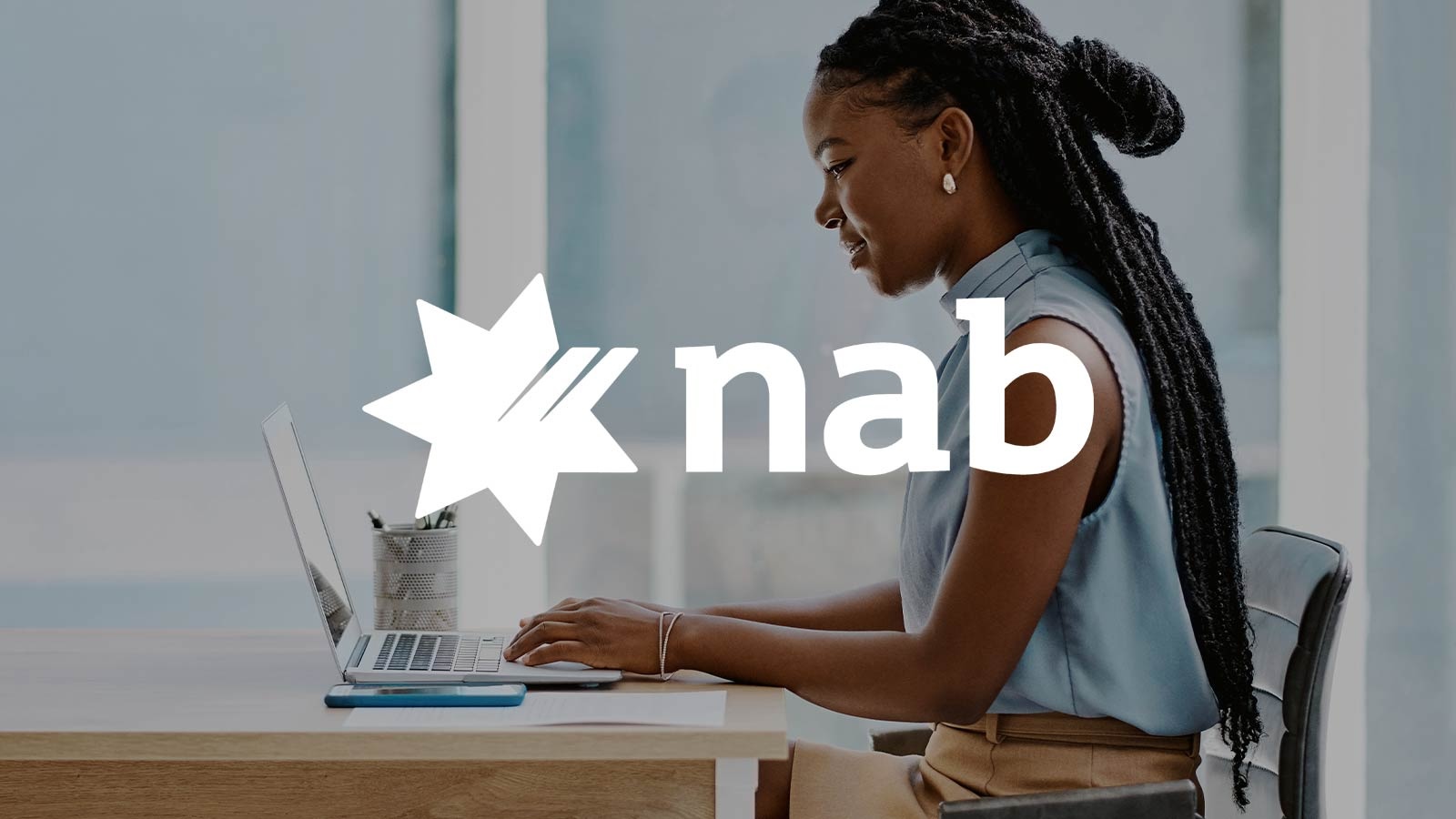 Person seated at a desk using a laptop, with a coffee cup nearby. The NAB logo featuring a star and the letters ‘nab’ is prominently displayed in the center of the image