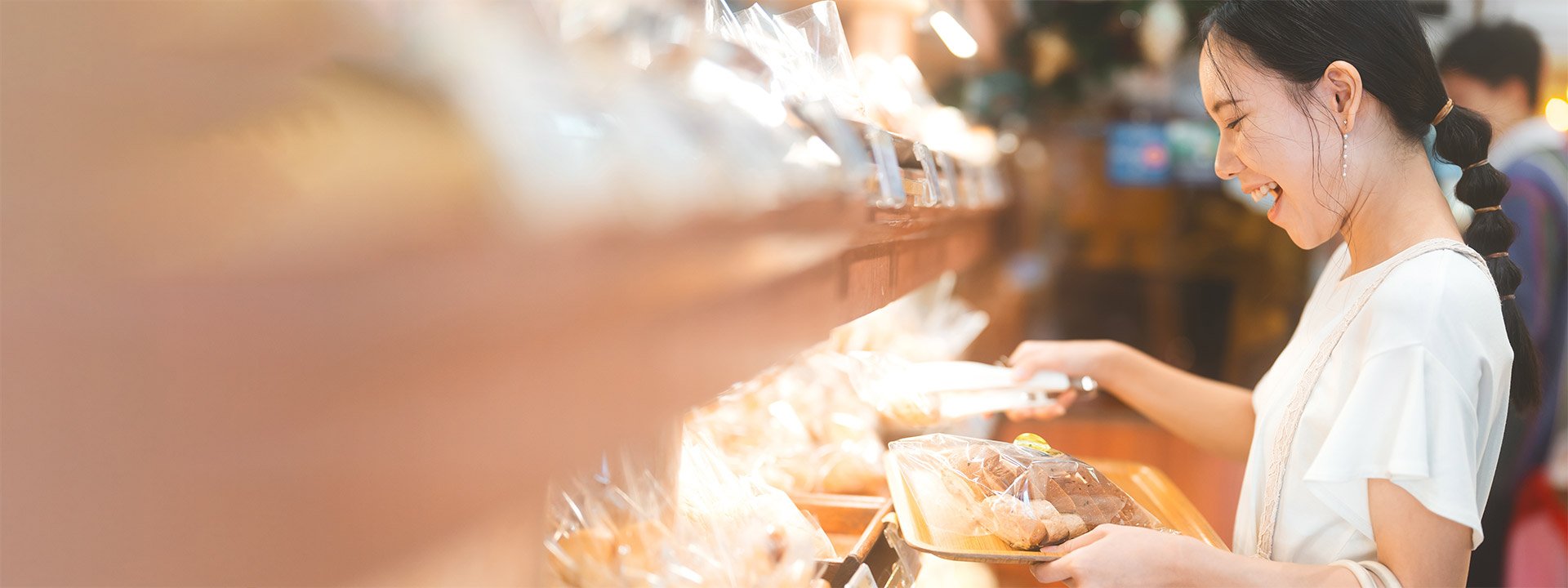 Happy smiling customer asian woman choosing whole grain bread at bakery shop