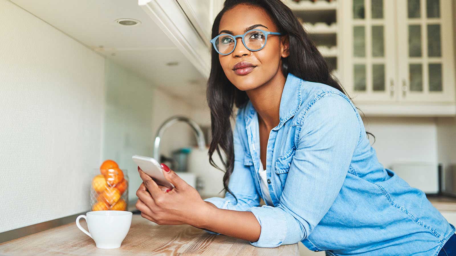 A smiling woman in her kitchen holds her phone.