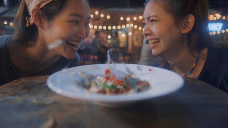 Two young ladies laughing in a restaurant in front of a dish, where they can pay for their order with a travel payment card from Visa.