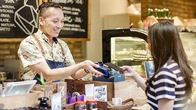 Women paying through mobilephone over electronic reader at cafe counter