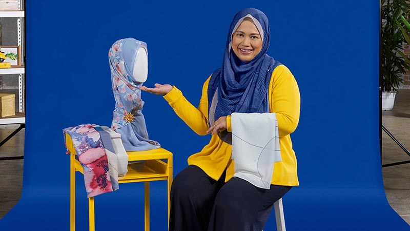 A woman wearing a yellow shirt and blue hijab sits on a chair, promoting help for small businesses. 