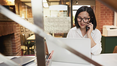 Portrait of young Asian businesswoman speaking by phone while working in modern office, copy space